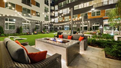 Luxurious apartment courtyard featuring cozy fire pit, stylish seating with vibrant cushions, and ambient string lights for a welcoming atmosphere.