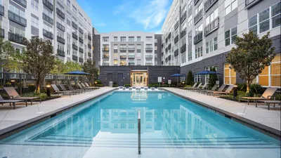 Luxurious apartment complex featuring a sparkling outdoor pool surrounded by comfortable lounge chairs and lush greenery, perfect for relaxation and leisure.