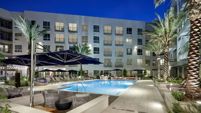 Contemporary apartment complex with a luxurious illuminated pool area, surrounded by palm trees and modern lounge seating, perfect for relaxation.