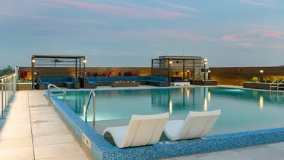 Elegant rooftop pool area featuring cozy cabanas, modern lounge chairs, and ambient lighting against a serene sunset backdrop.