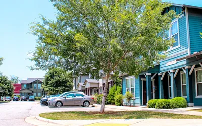 Charming suburban neighborhood with colorful townhouses, vibrant greenery, and ample parking space under a clear blue sky.