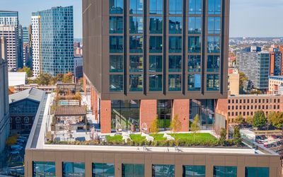Modern cityscape view showcasing a sleek high-rise building with rooftop gardens and lush greenery, set against a vibrant urban skyline.