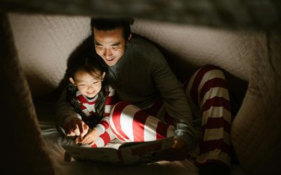 Cozy family moment inside a blanket fort, featuring a smiling parent and child in matching striped pajamas enjoying a bedtime story together.