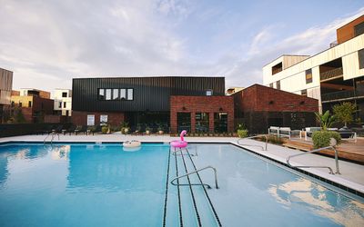 Modern apartment complex with sleek architecture featuring a refreshing swimming pool, surrounded by stylish brick and black finished buildings. Perfect for luxury living and leisure.