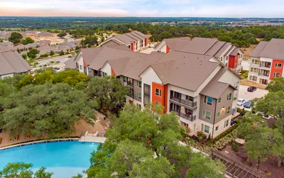 Aerial view of modern apartment complex with colorful facades surrounded by lush greenery and a sparkling swimming pool, offering a serene and vibrant living environment.