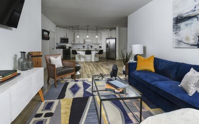 Modern open-concept living room with vibrant blue sofa, stylish geometric rug, and elegant kitchen featuring contemporary white cabinetry.