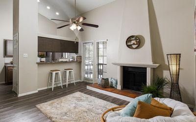 Inviting living room with a vaulted ceiling, cozy fireplace, and a modern kitchen with a breakfast bar.