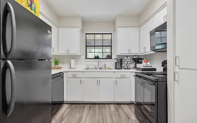 Contemporary kitchen with sleek black appliances, crisp white cabinetry, and elegant wood flooring, perfect for culinary creativity.