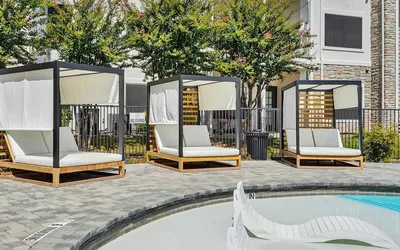 Inviting poolside cabanas with plush seating set against lush gardens, perfect for relaxation in a modern apartment setting.