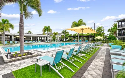 Large resort-style pool with shallow entry areas, surrounded by lounge chairs, umbrellas, and palm trees.