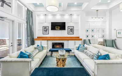 Luxurious clubhouse with chic white sofas, vibrant blue accents, modern fireplace, and elegant decor in a bright, open-concept space.