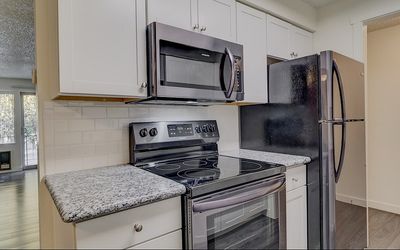 Modern kitchen with stainless steel appliances, granite countertops, and open space leading to a bright living area with large windows.
