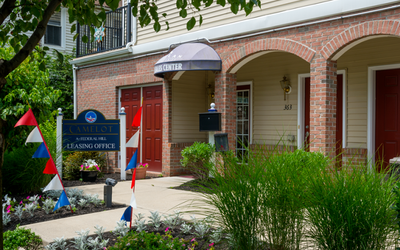 Inviting leasing office entrance at Camelot with vibrant signage and lush landscaping.