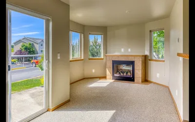 Bright and inviting living room with large windows and cozy fireplace, offering serene views of the neighborhood.
