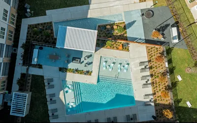 Aerial view of a chic luxury apartment complex featuring a crystal-clear swimming pool with reclining sun loungers, stylish cabanas, and beautifully landscaped gardens.