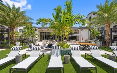 Luxurious outdoor lounge area featuring sleek sun loungers, lush greenery, and modern patio furniture in a resort-style setting.