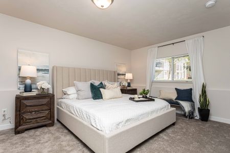 Spacious Master Bedroom with brand new plush creme carpet, a large window with natural lighting and two tone paint. Bedroom has a kind size platform bed, 2 night stands, and a decorative bench under the window with decorative pillows.