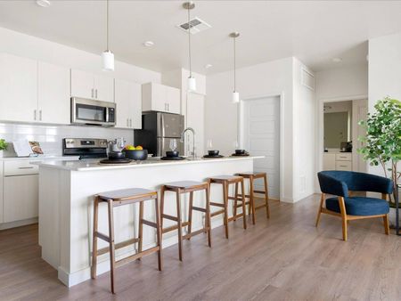 Glendale Apartments - Acero At the Stadium - Kitchen With Long Island, Four Stools, White Cabinets, And Appliances.