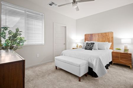 One, Two, And Three-Bedroom Apartments In Queen Creek, AZ - Acero Harvest Station - Spacious Bedroom With Plush Carpeting, Bright Walls, A Large Window To Let Plenty Of Light, And A Ceiling Fan. A Full-Size Bed Sits In The Center Of The Room With Plenty Of Space On All Sides