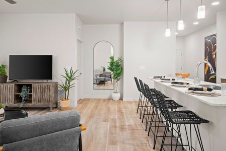 Pet Friendly Apartments in Queen Creek AZ - Acero Harvest Station - Living Area View From Corner Of Large Sectional Couch Facing Towards And Entertainment Center With A Tv In Front Of Bright White Walls, The Kitchen Can Be Seen In The Background Thanks To Spacious Open Floor Plans