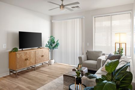 Pet-Friendly Apartments In Goodyear, AZ - Acero Roosevelt - A Spacious And Bright Living Area With Wood Flooring, A Ceiling Fan, And A Sliding Glass Door That Leads Outside. The Room Has A Couch And A Chair With A Few Ottomans Facing Towards A Television
