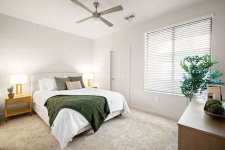 1, 2, & 3-BR Apartments In Goodyear, AZ - Acero Roosevelt - A Bright And Spacious Bedroom With A Queen Sized Bed. The Room Has White Walls And Plush Carpeting And Features A Large Window And A Ceiling Fan Above The Bed
