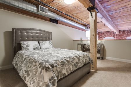 View of Bedroom, Showing Furnishings and Loft-Style Layout, Wooden Beam, View of Brick Wall at Alpha Mill Apartments