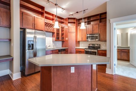 View of Kitchen, Showing Island, Stainless Steel Appliances, Plank Wood Flooring, and View of Bathroom at Alpha Mill Apartments