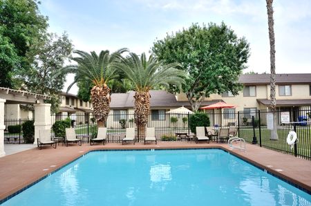 View of Resort-Style Pool, Showing Sundeck, Seating With Umbrellas, and Landscaping at Camelot Apartments