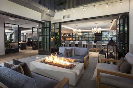 Closeup of fire table with lounge tables and indoor clubroom in the background at Modera San Diego apartments.
