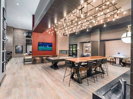 Light installation above bar top tables next to a pool table and arcade game area with kitchen space