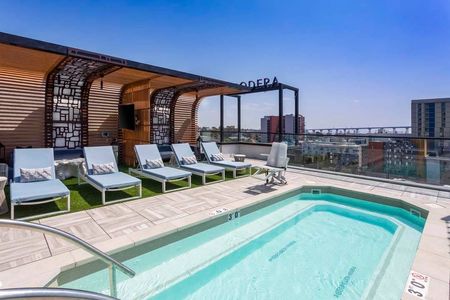Rooftop pool with chaise lounge seating, shade structures, and a clear railing that allows for stunning city and bay views at Modera San Diego apartments.