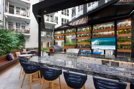Outdoor kitchen with brick pizza oven and grilling station in outdoor bar area with vertical greenery and TV at Modera San Diego apartments