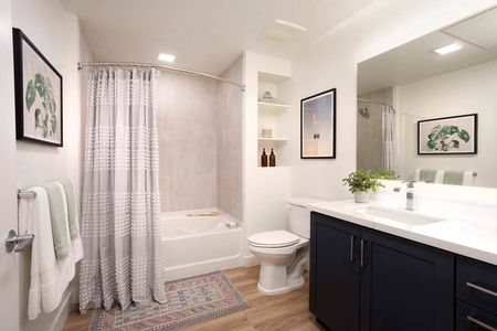 Bathroom with large mirror, countertops and floor-to-ceiling tile in shower with soaking tub at a Modera San Diego apartment.