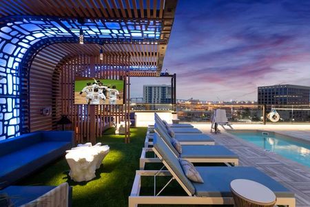 Chaise lounge and sofa seating areas illuminated by hip lighting and outdoor TVs near the pool at Modera San Diego apartments.