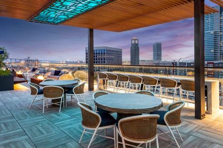 A line of rooftop fire pits, seating that faces the city views, and outdoor dining tables facing city and bay views at night at Modera San Diego apartments.