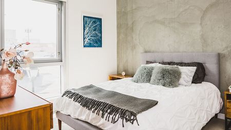 Bedroom with white and grey bedding against a concrete wall