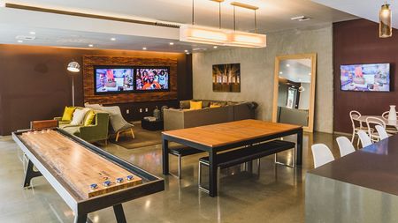 Resident lounge with table, shuffleboard, and seating to view flat screen televisions