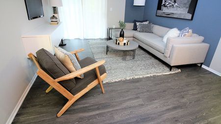 Living Room with Couch and Accent Chair featuring Faux Wood Style Flooring in an Alister Town Center apartment.
