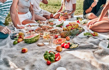 Stock photograph of people gathered around a picnic blanket covered with food and drinks.