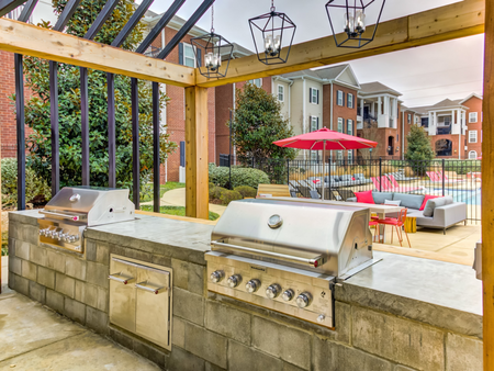 Outdoor lounge at our apartments in Tuscaloosa, featuring two grills, a shade structure, and outdoor chairs.