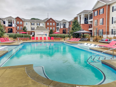 The pool area at our apartments in Tuscaloosa, featuring red pool chairs, umbrellas, and a clubhouse.