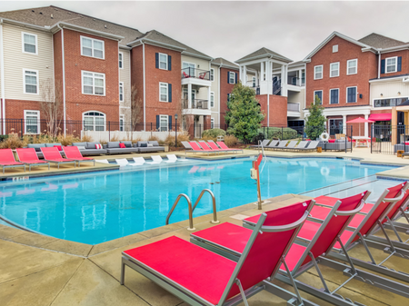 The pool area at our apartments in Tuscaloosa, featuring red pool chairs, umbrellas, and a clubhouse.