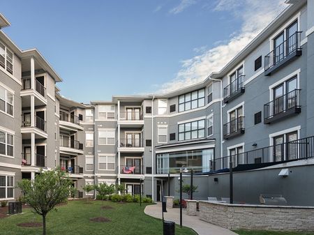 Courtyard with apartments overlooking the greenery, trees, and seating around the community.