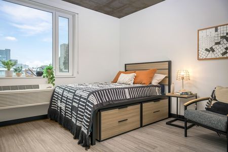 Model apartment bedroom including light wood grain furniture with black frames and a window overlooking Eugene