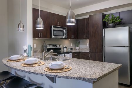 Model apartment kitchen with dark cabinets, granite countertops, and stainless steel appliances