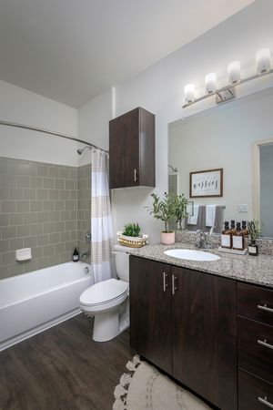 Model apartment bathroom with dark wood cabinets, granite countertops, and hard wood style flooring