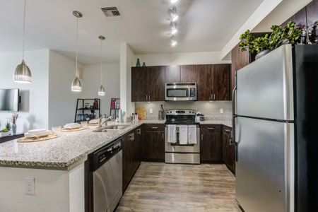 Model apartment kitchen with hard wood style flooring, dark brown cabinets, and stainless steel appliances
