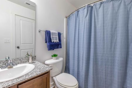 Model apartment bathroom with brown cabinetry, granite countertops, and white bathroom facilities