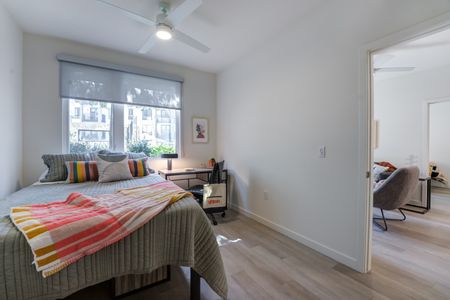 Model apartment bedroom with light hardwood flooring, white walls, and a large window